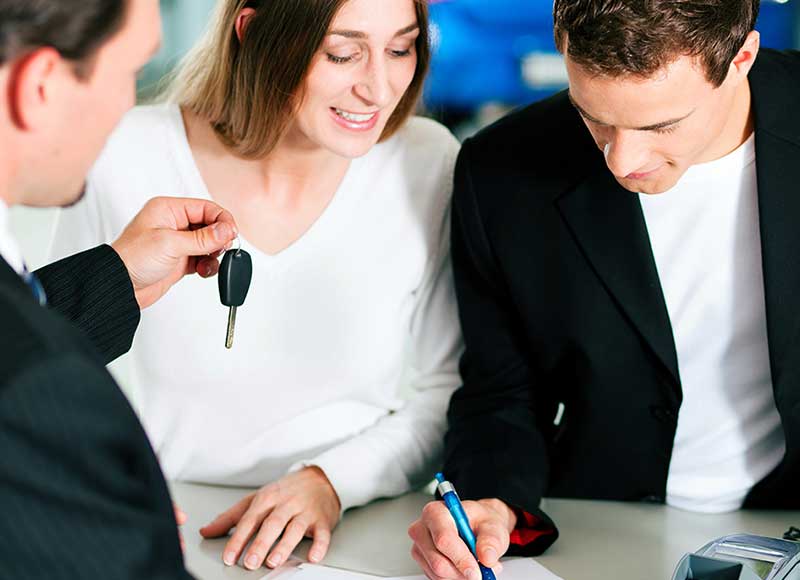 Couple signing papers as salesman hands over a key